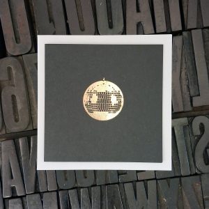 A picture of a shiny mirror ball printed on black card.
